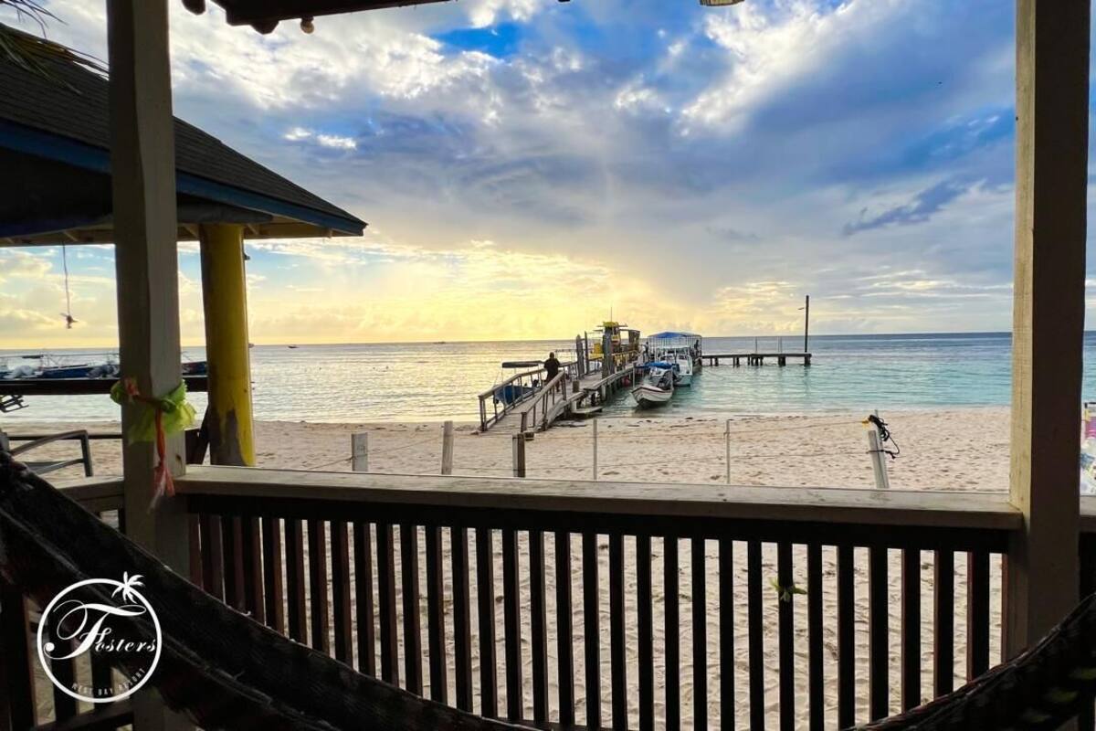 A beach view with a pier, boats, and a hammock on a wooden deck.