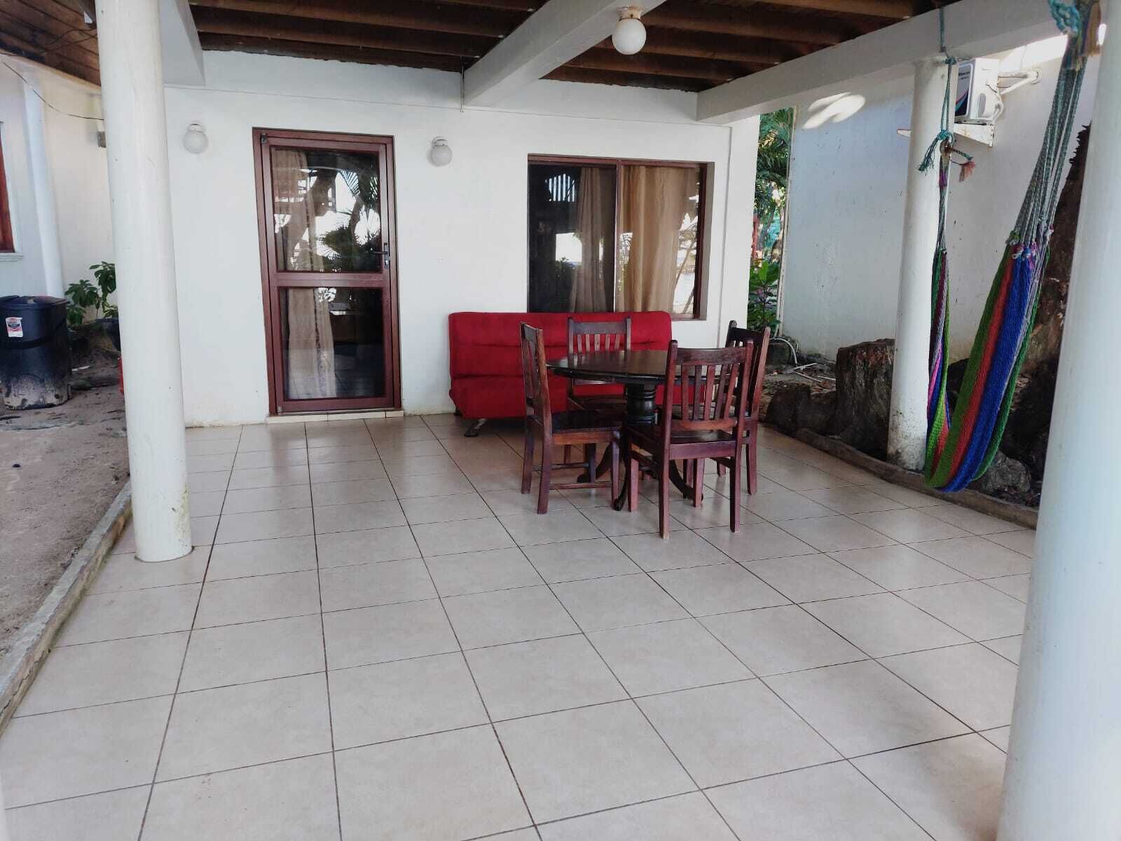 Un patio couvert comprenant une table et des chaises, un canapé rouge et un hamac.