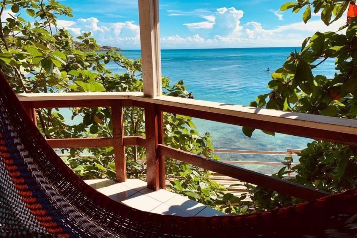A hammock on a balcony overlooking a clear blue sea with lush greenery.