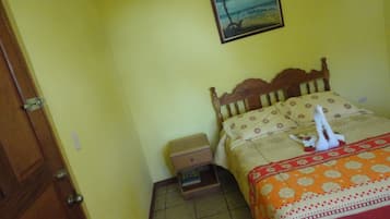 A small, simple room with a bed, a nightstand, and a wooden door.