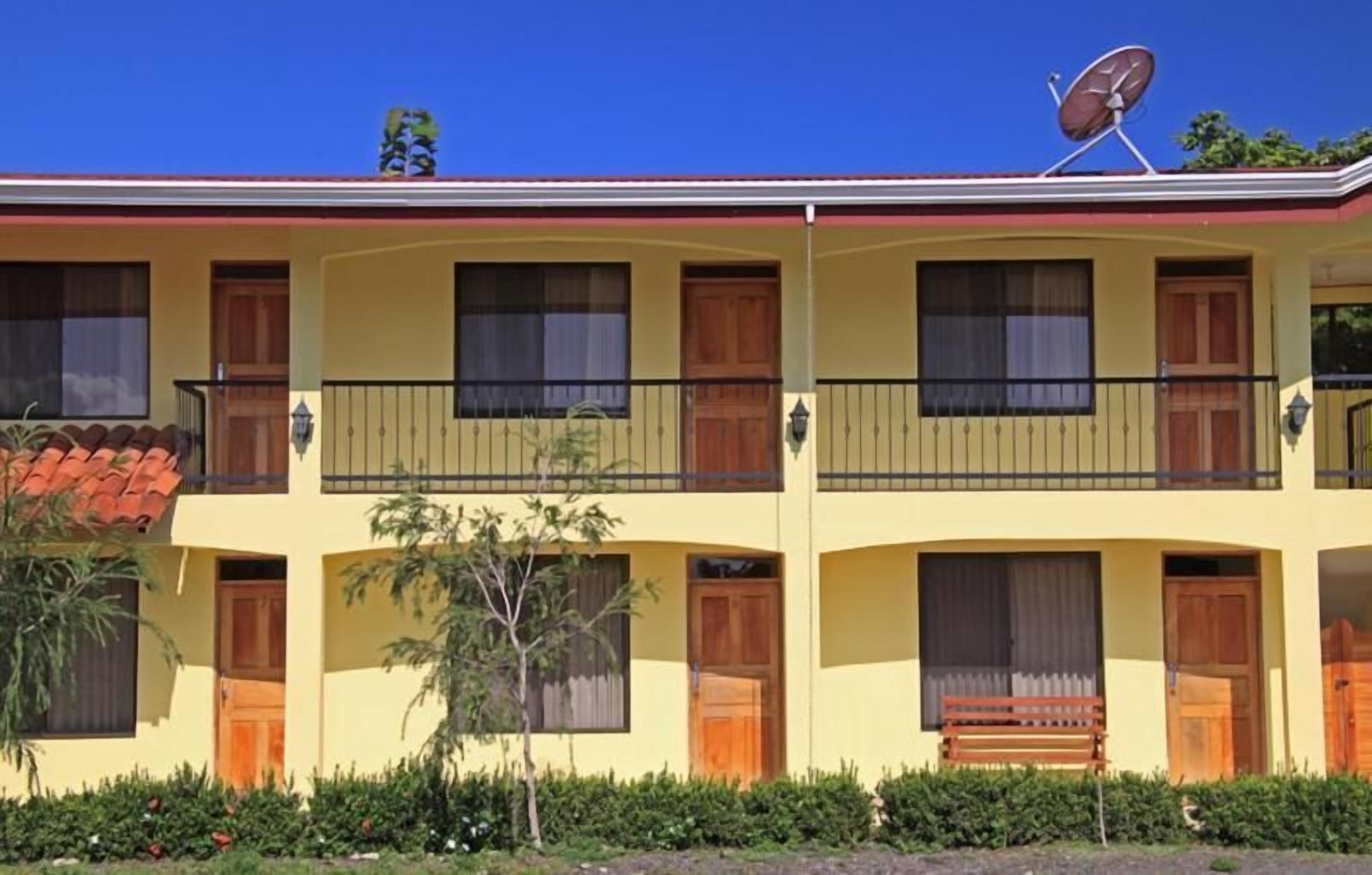A two-story building with balconies, a satellite dish, and a bench in front.