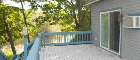 A wooden deck with a blue railing, a white door, and an air conditioning unit mounted on the wall.