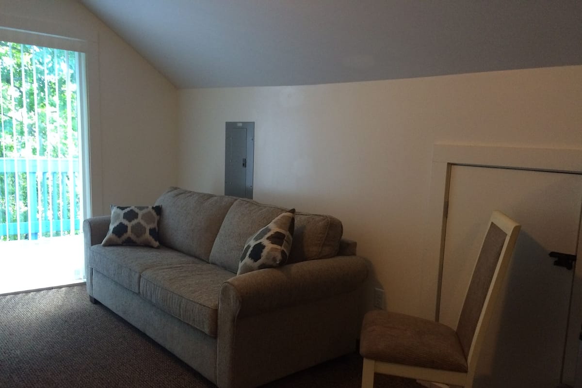 A living room with a sofa and a chair, a sliding glass door, and a door with a handle.
