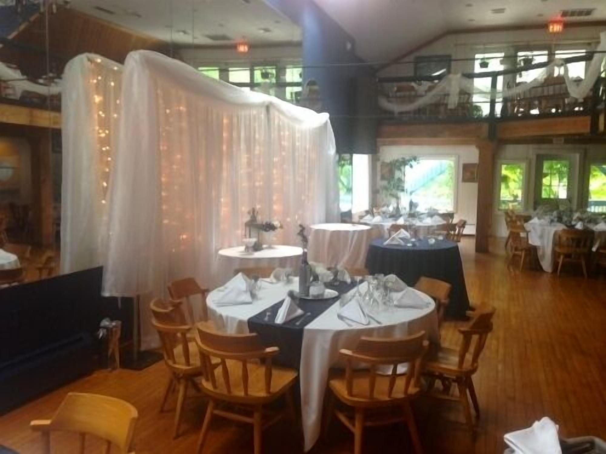 Un restaurant avec des tables rondes disposées pour le service, des chaises en bois et un plafond haut laissant entrer la lumière naturelle.