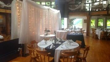 A restaurant with round tables set for dining, wooden chairs, and a high ceiling with natural light.