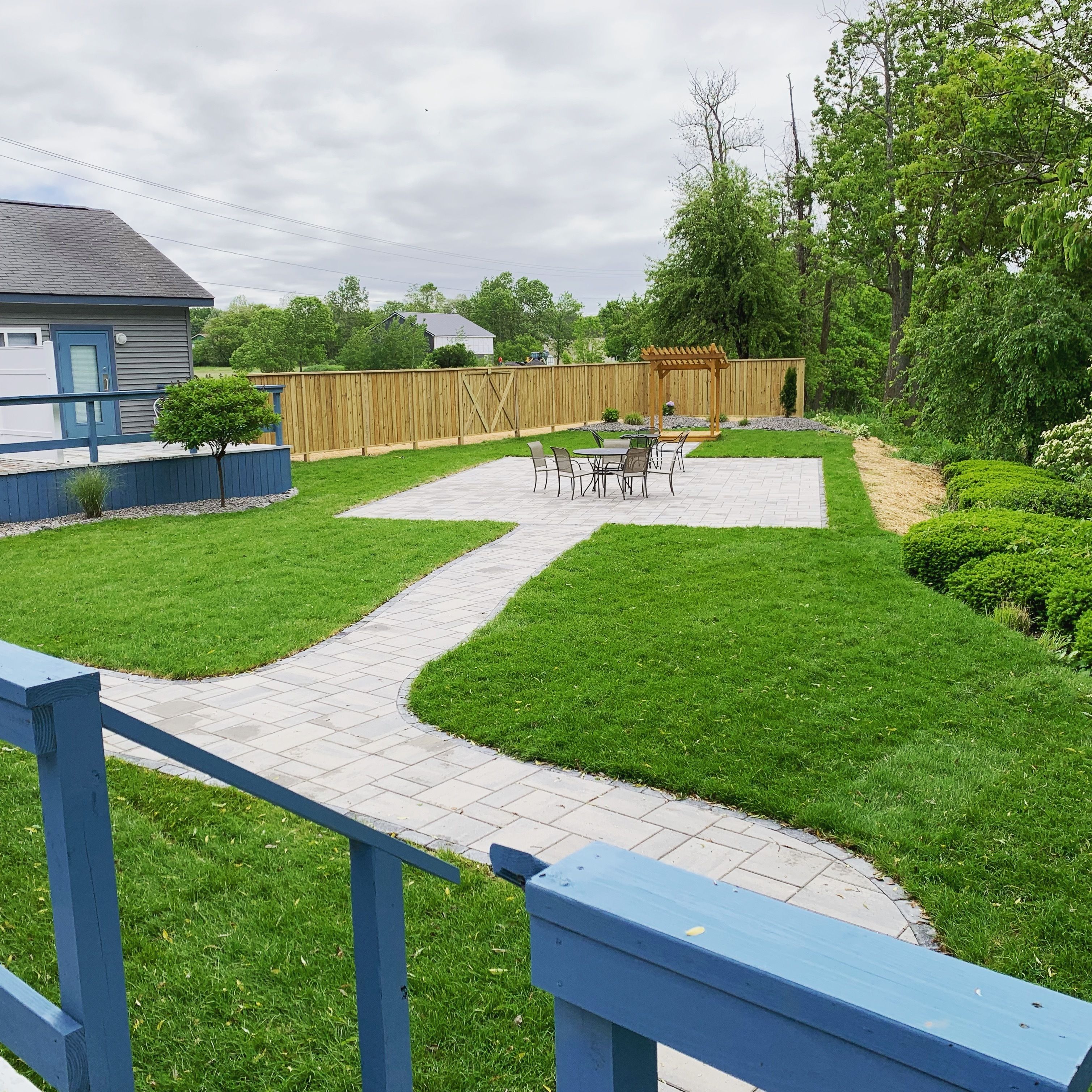 Un jardin avec une terrasse, une clôture en bois et un petit arbre.