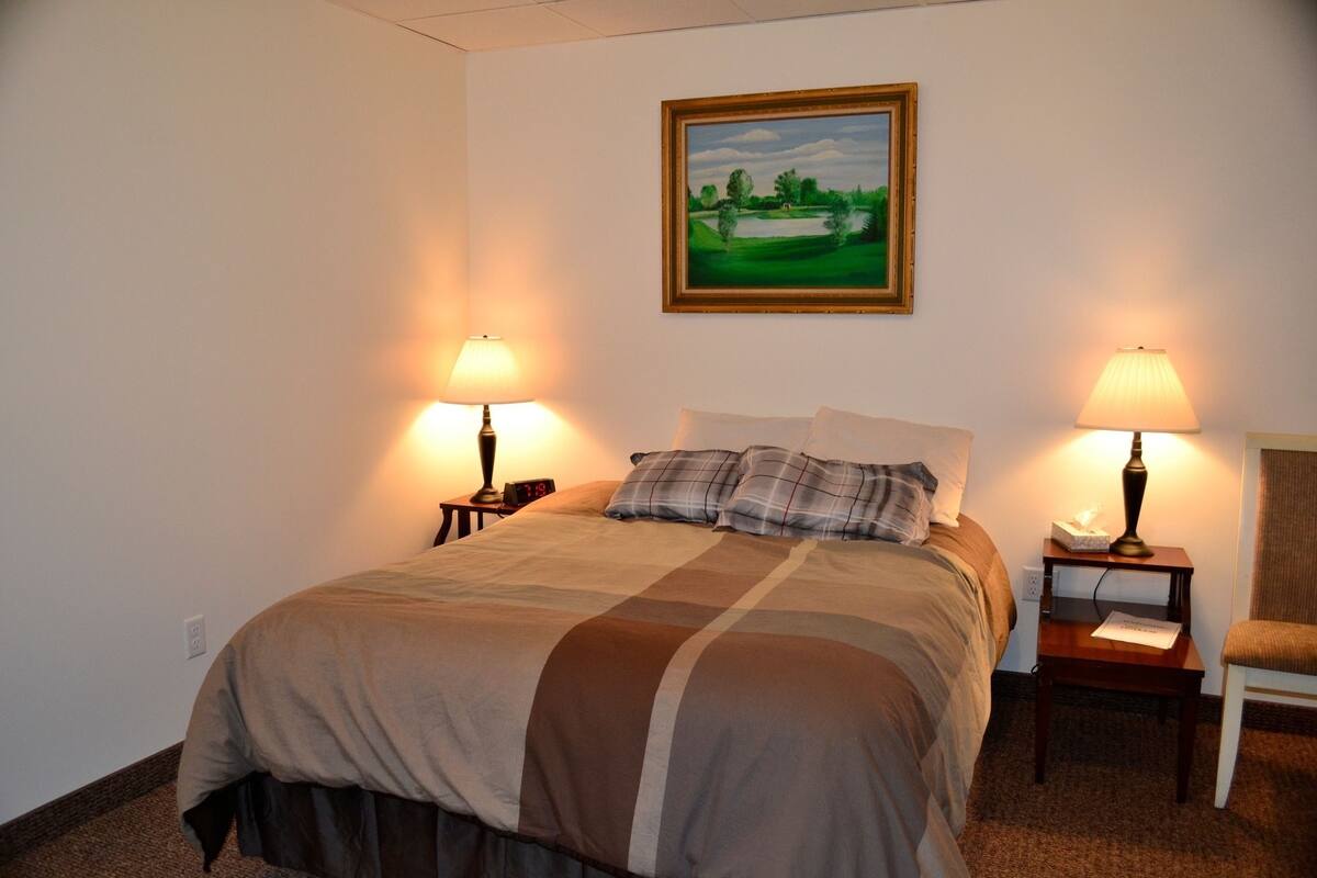 A hotel room with a large bed, two bedside tables with lamps, a chair, and a painting on the wall.