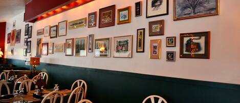 A restaurant with multiple tables and chairs, a wall adorned with framed artwork, and a green and red color scheme.