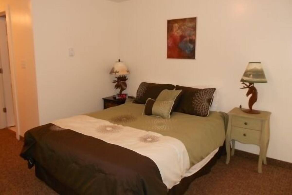 A bedroom with a bed, two bedside tables, a lamp, and a painting on the wall.