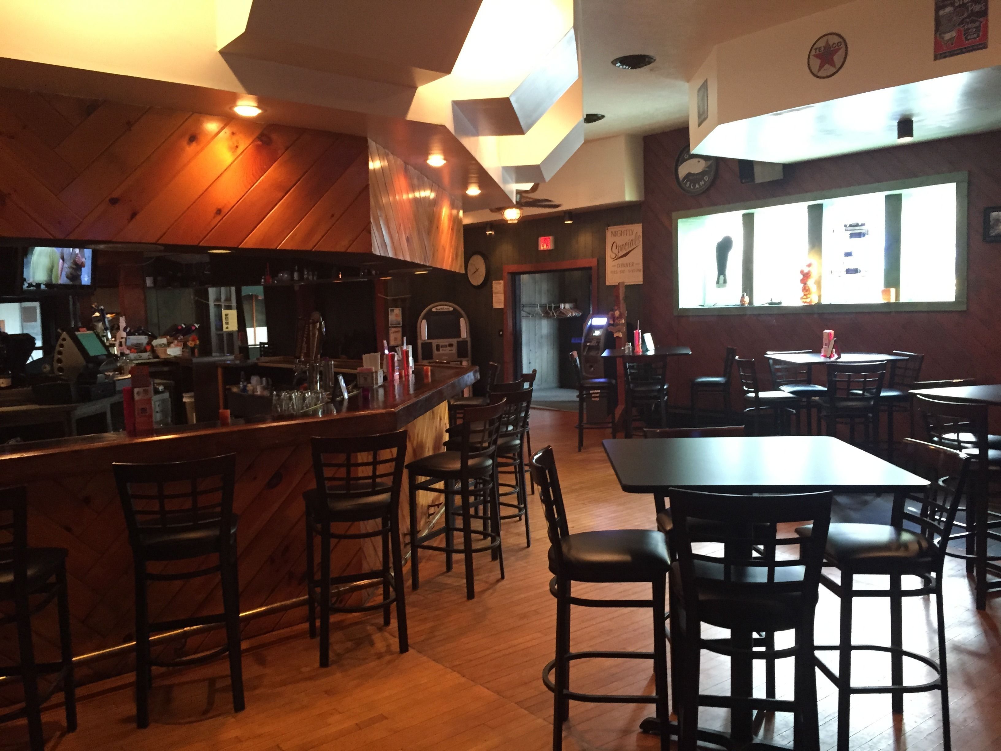 Interior d'un restaurant amb zona de bar, parets de fusta i diverses taules i cadires.