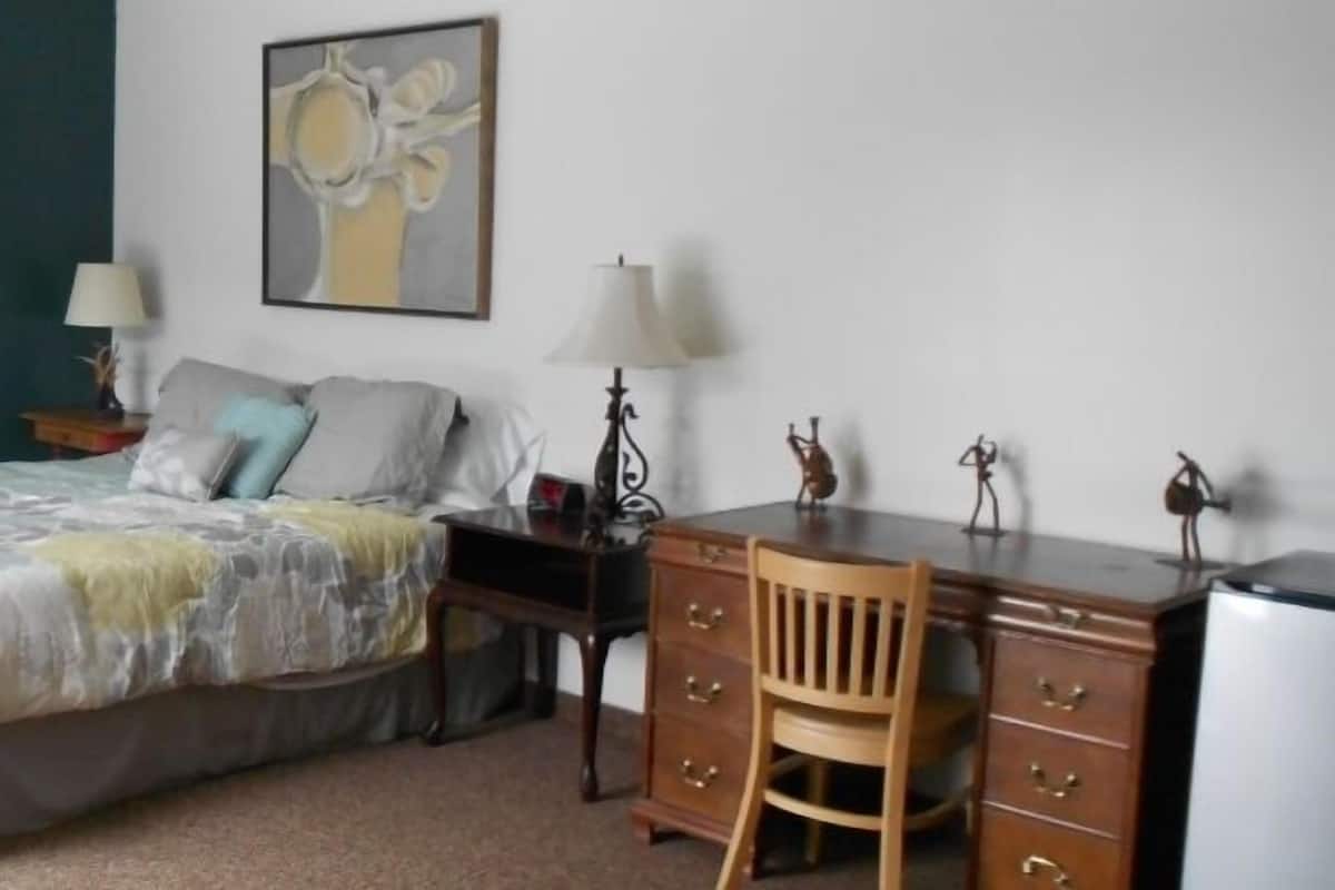 A bedroom with a bed, a desk, a chair, a dresser, and two wall-mounted lamps.