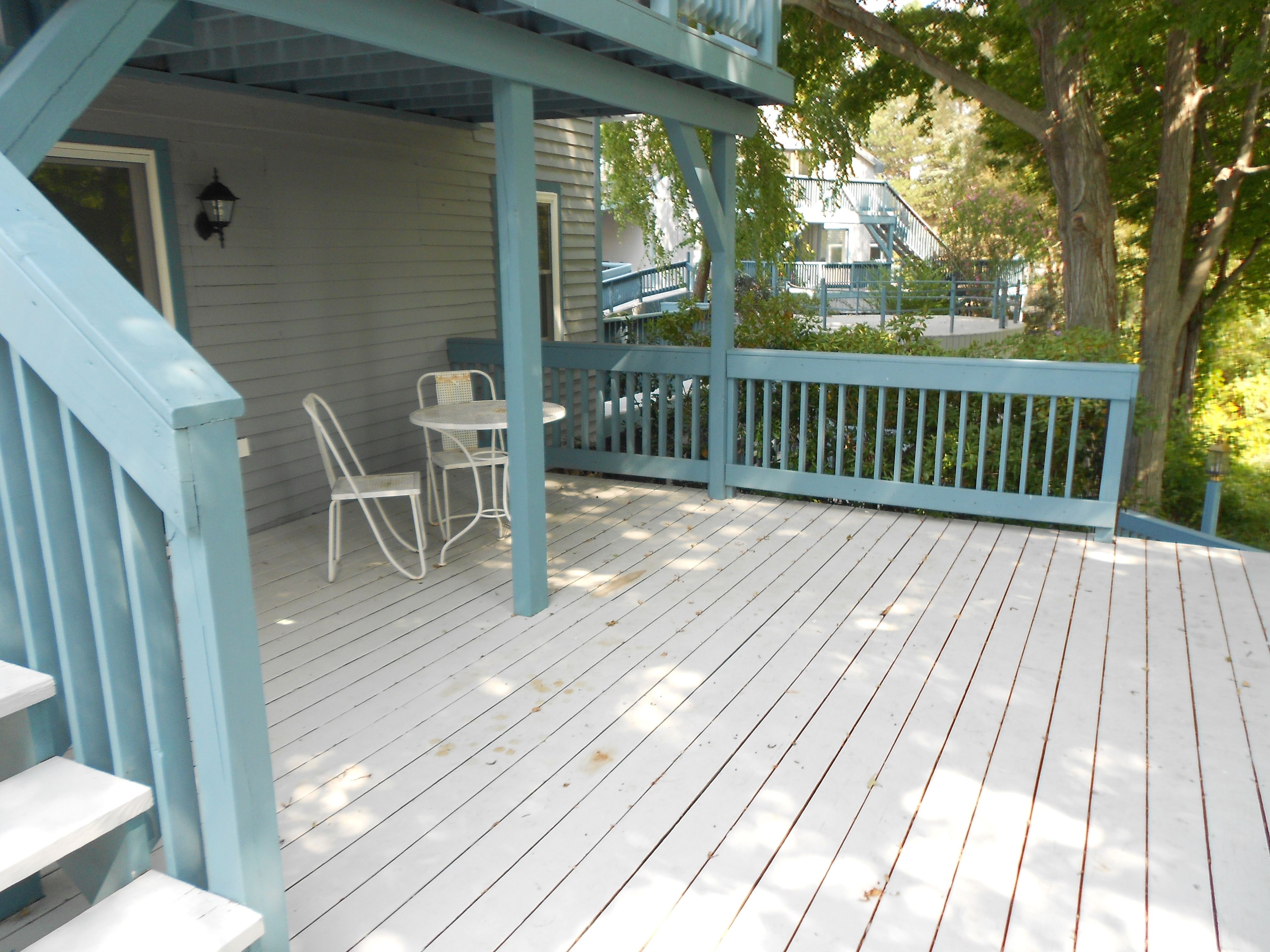 A wooden deck with white chairs and a blue railing.
