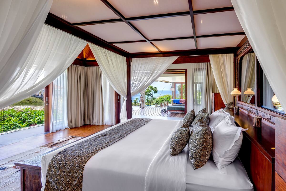 A spacious bedroom with a large bed, a wooden headboard, and a view of the outdoors.