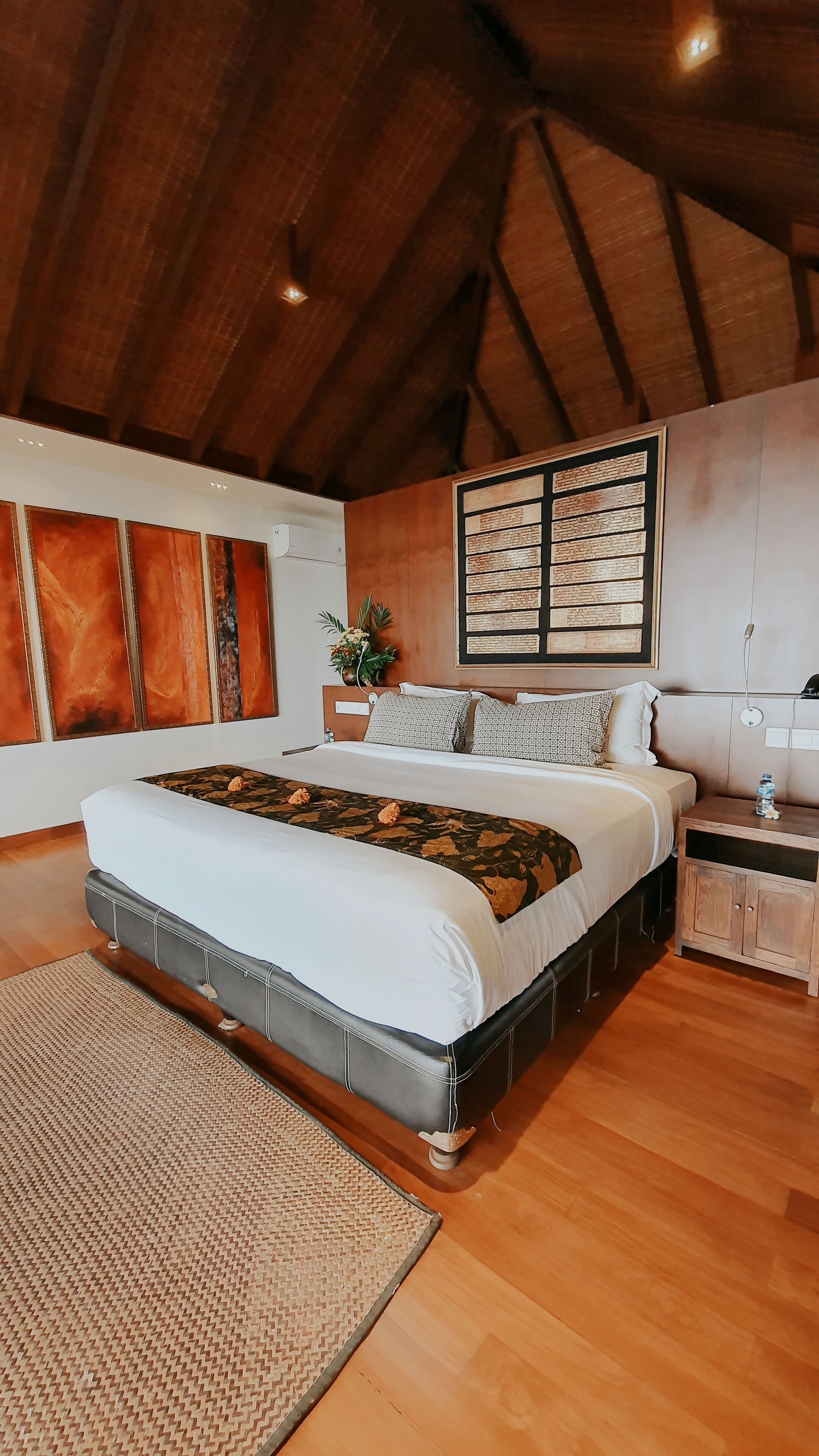 A spacious bedroom with a large bed, wooden ceiling beams, and a wall-mounted artwork.