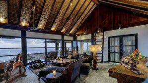 A spacious living area with a view of the ocean, wooden ceiling, and a rustic table centerpiece. - Private Villas of Bali (Kutuh)