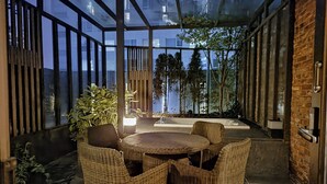 A glass-enclosed patio with wicker furniture, a potted plant, and a view of a building. - MD HOTEL DONGTAN (Hwaseong)