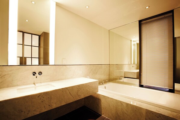 Un baño moderno con un lavamanos de mármol, una bañera y un espejo grande.