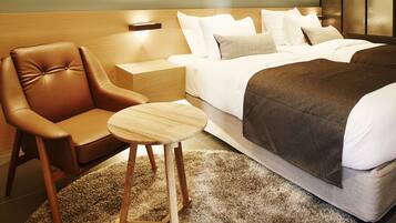 A modern hotel room with a bed, a leather armchair, a small wooden table, and a textured rug.