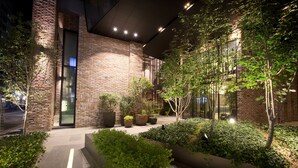 A modern building with brick walls, large windows, and a well-lit outdoor area with plants and a pathway. - MD HOTEL DONGTAN (Hwaseong)