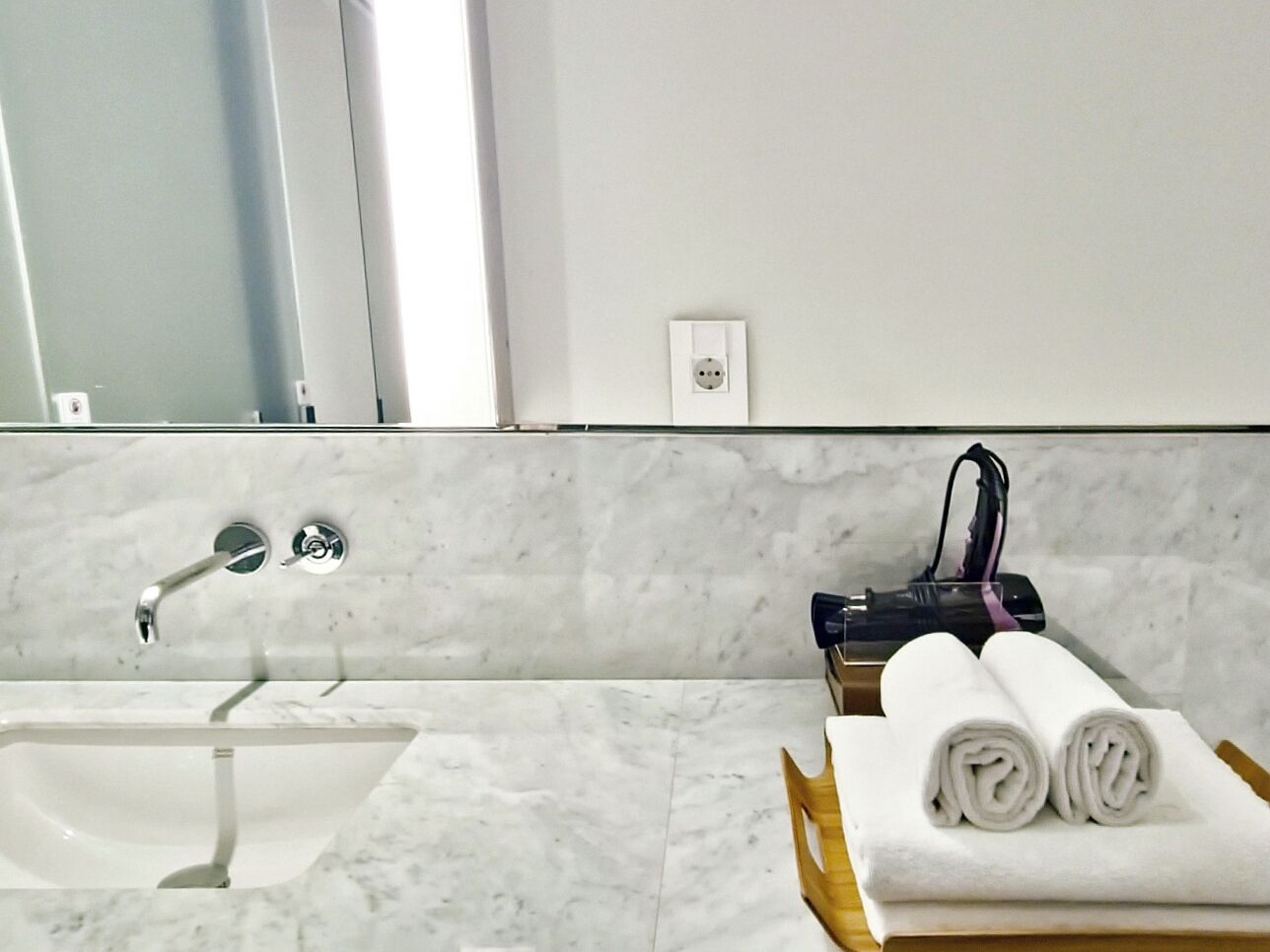 A bathroom with a sink, mirror, towel rack, and a power outlet.