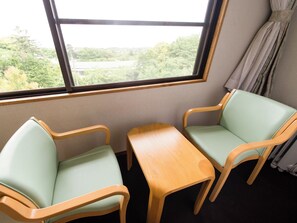 A room with two light green chairs and a wooden table, a window with a view of greenery and buildings, and a curtain on the right. - LiVEMAX RESORT Izu-kogen (Ito)