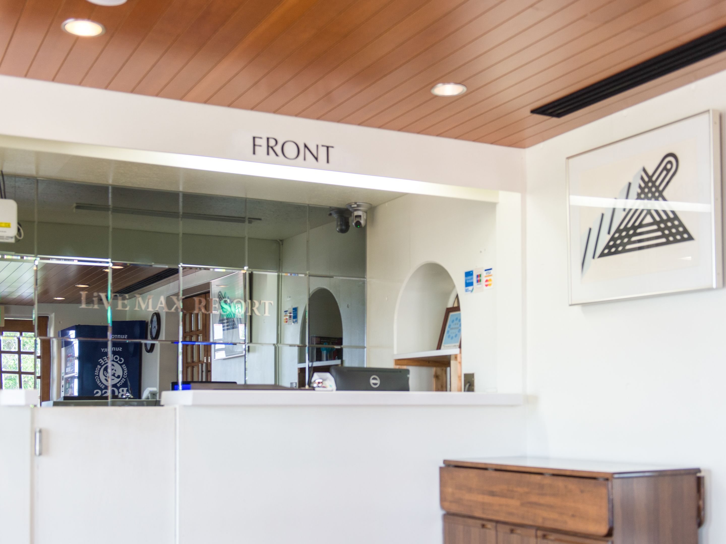 Uma área de recepção com um letreiro 'FRONT', uma divisória de vidro, uma mesa de madeira e uma obra de arte emoldurada na parede.