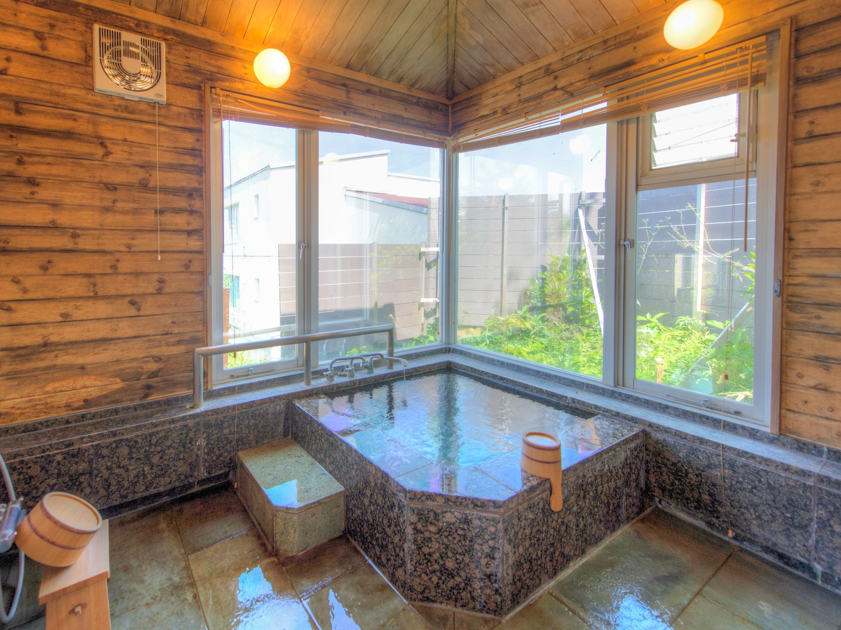 A wooden interior with a hot spring bath, large windows, and a view of the outside.