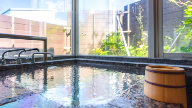 A spa area with a hot tub, a wooden barrel, and a view of a brick wall and greenery outside. - Livemax Resort Itokawana (Ito)