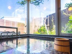 A spa area with a hot tub, a wooden barrel, and a view of a brick wall and greenery outside. - Livemax Resort Itokawana (Ito)