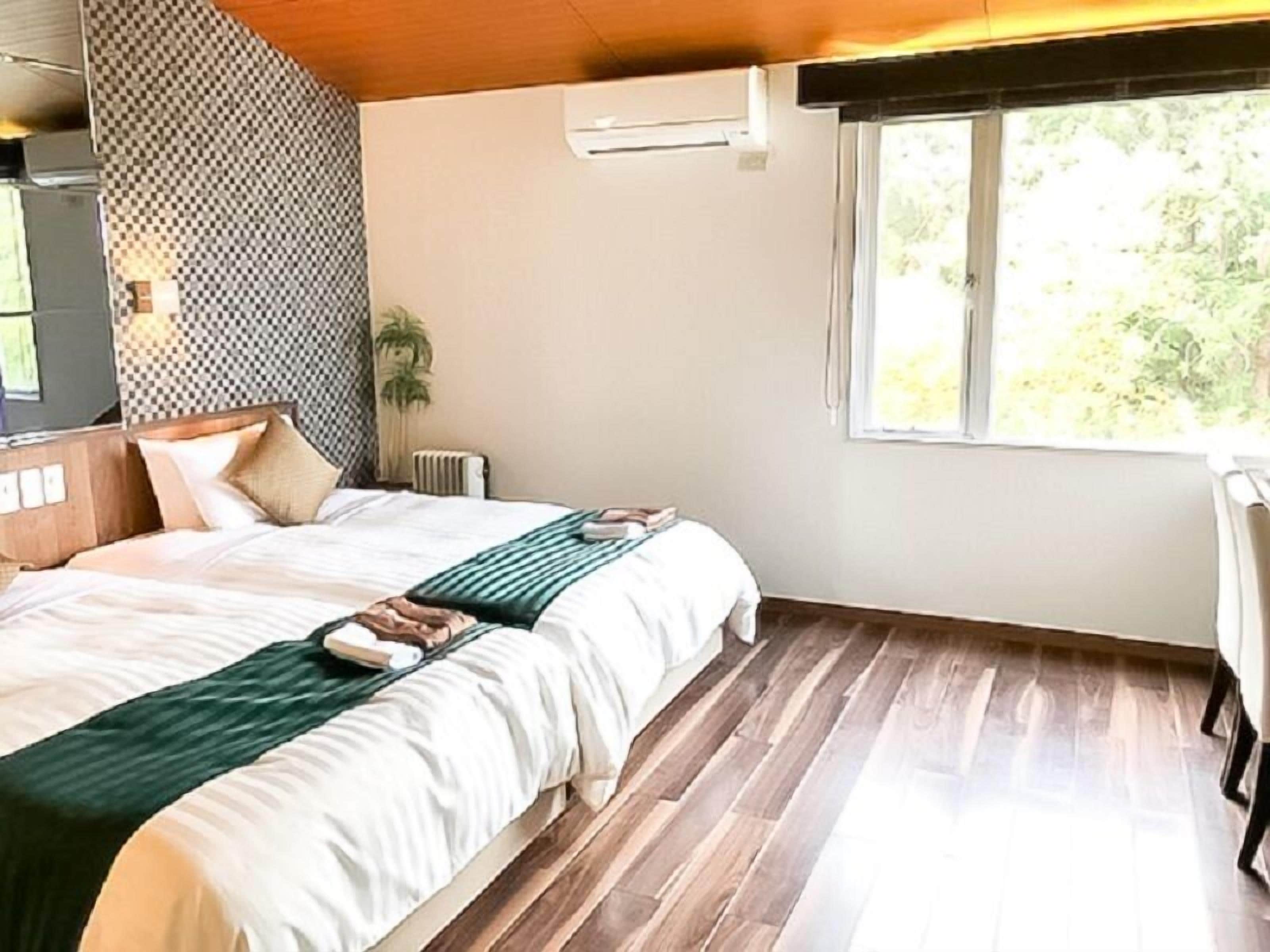 A bedroom with a large bed, a window with a view of greenery, and a patterned wall.