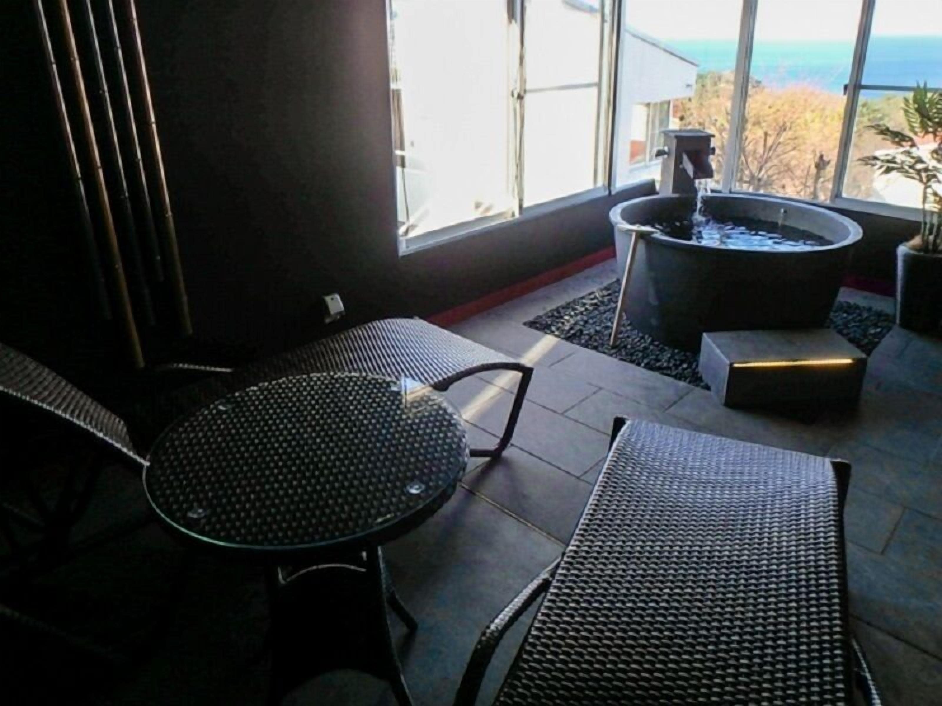 A sunlit patio with a hot tub, two wicker lounge chairs, and a small table.