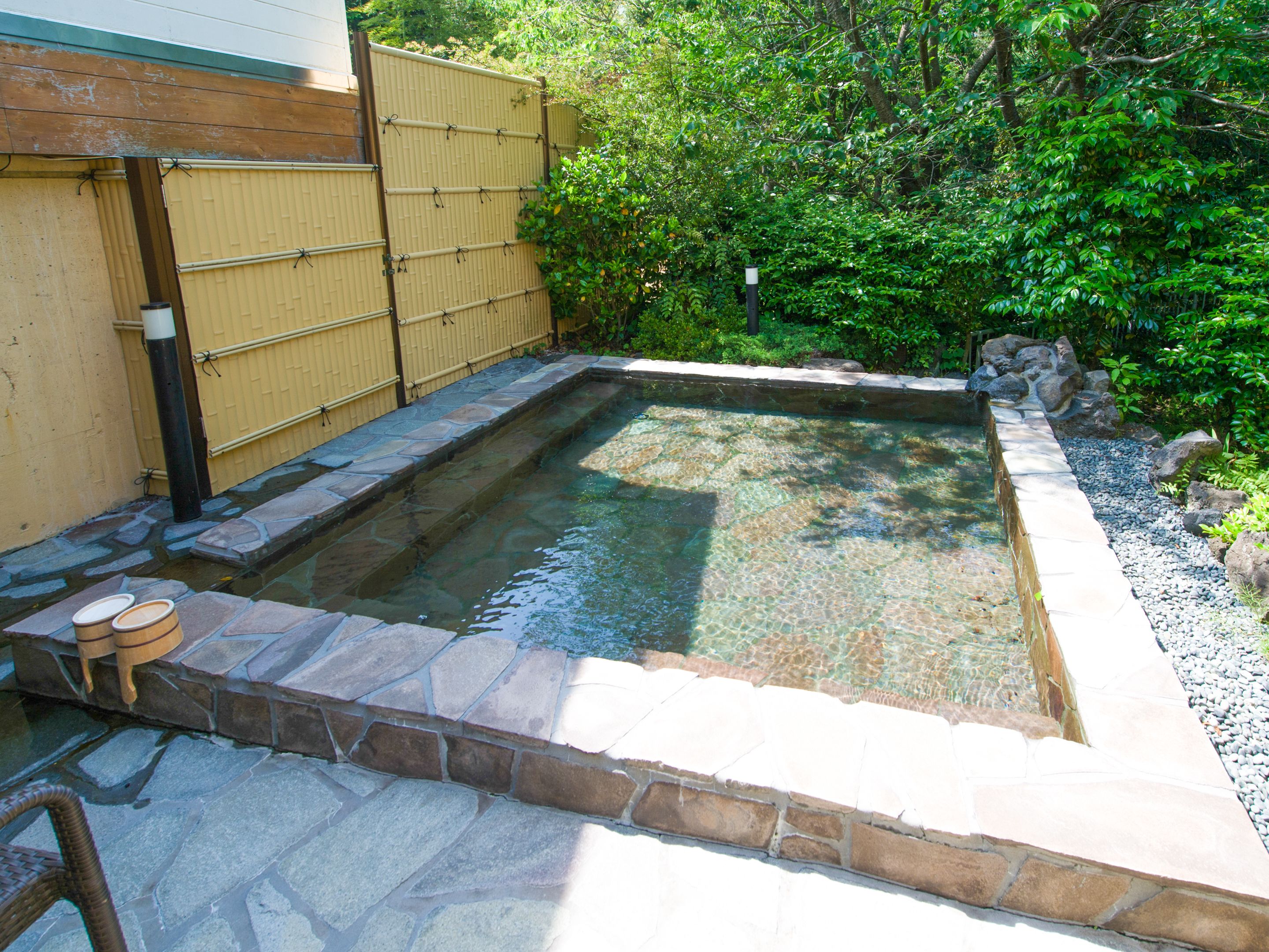 Una piscina rectangular con bordes de piedra, rodeada por una valla de bambú y abundante vegetación.