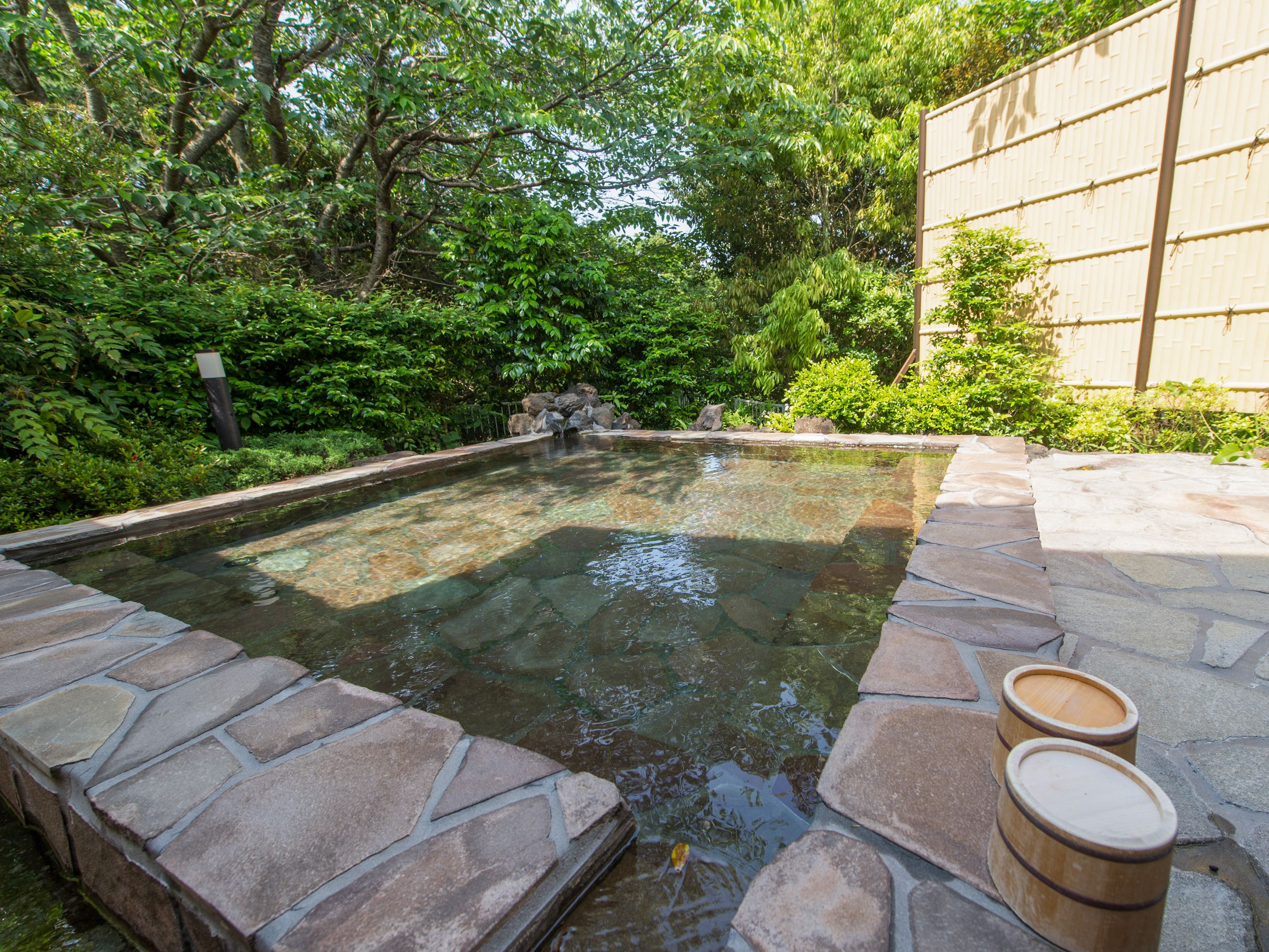A stone-lined pool with a wooden structure on one side, surrounded by lush greenery.