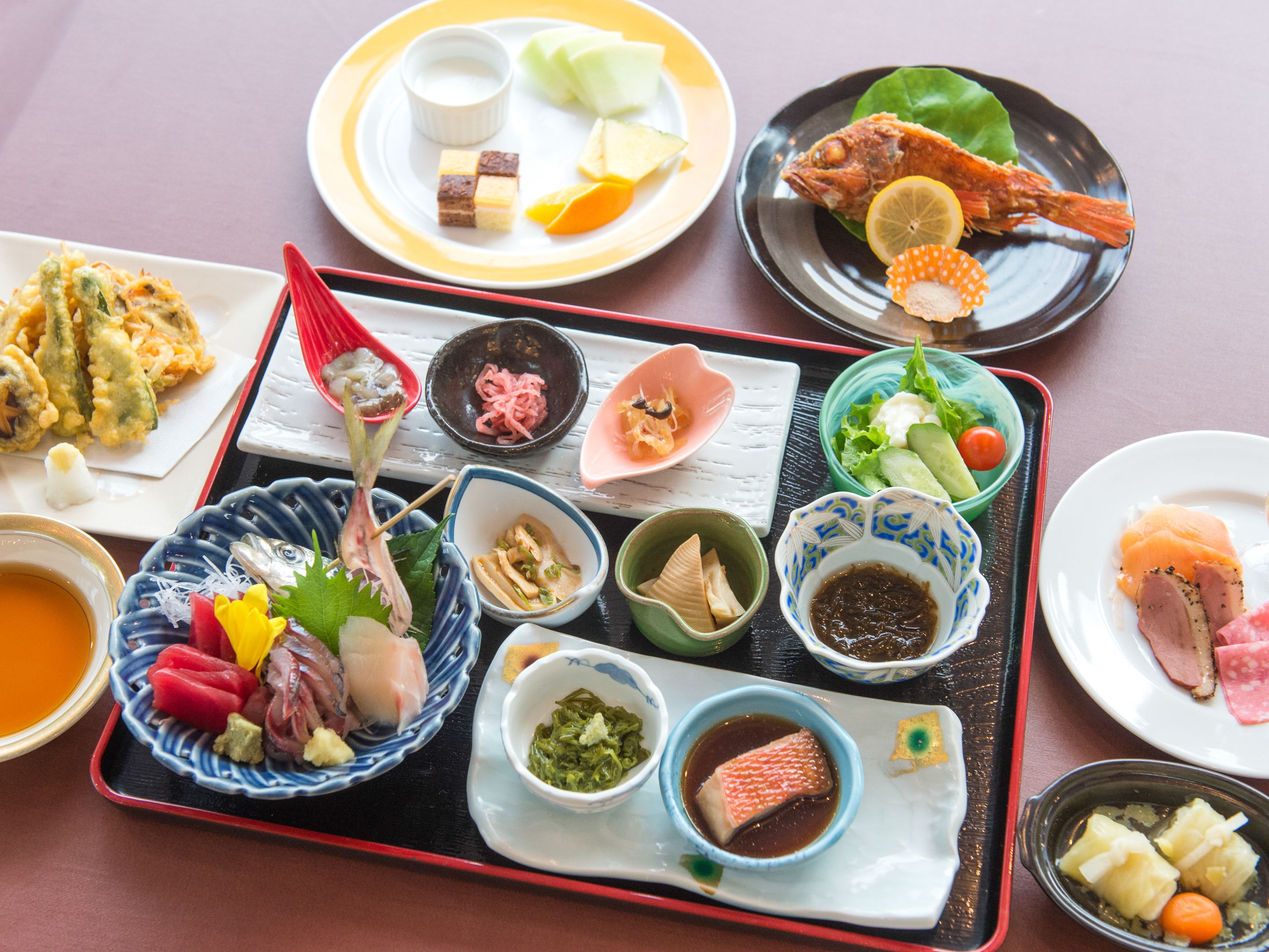 A variety of Japanese dishes arranged on a tray, including sushi, sashimi, and tempura.
