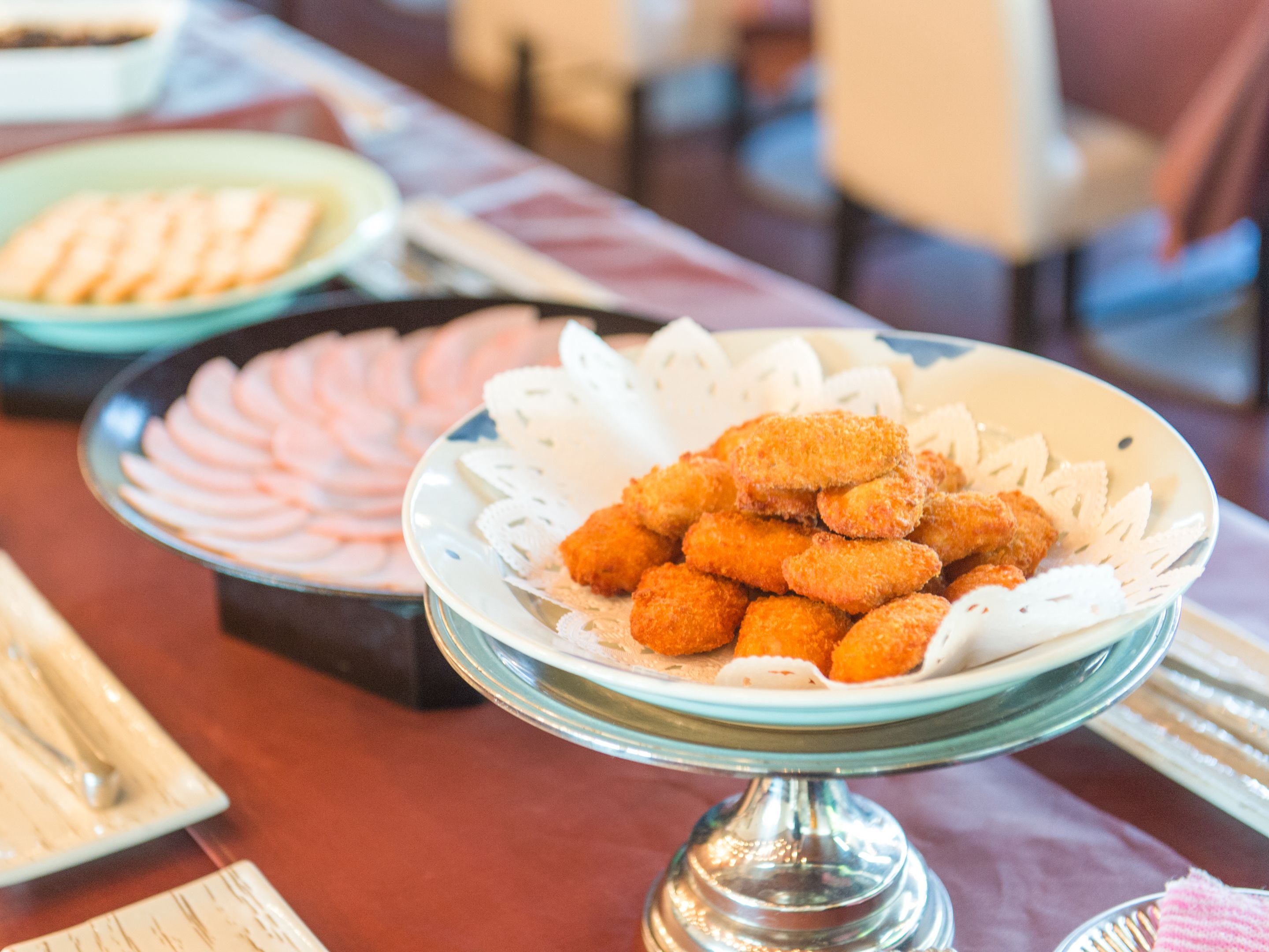 Ein reichhaltiges Buffet mit verschiedenen Speisen, darunter eine Schüssel paniertes Hähnchenfleisch und ein Teller Obstspalten.