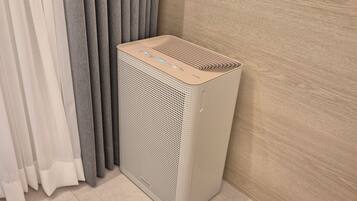 A portable air purifier in a corner of a room with a light-colored floor and a wooden wall.