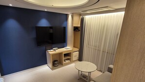 A modern hotel room with a large flat-screen TV mounted on the wall, a small round table, a sofa, and a built-in wardrobe with a mirror. - Hound Hotel Gwangju Cheomdan (Gwangju)