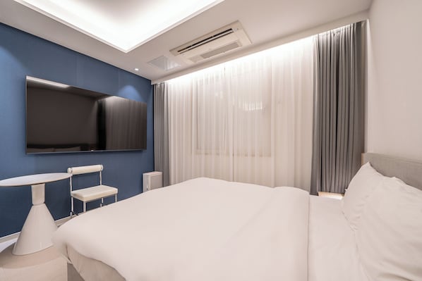 A modern hotel room with a bed, a desk, a chair, a TV, and a large window with curtains.