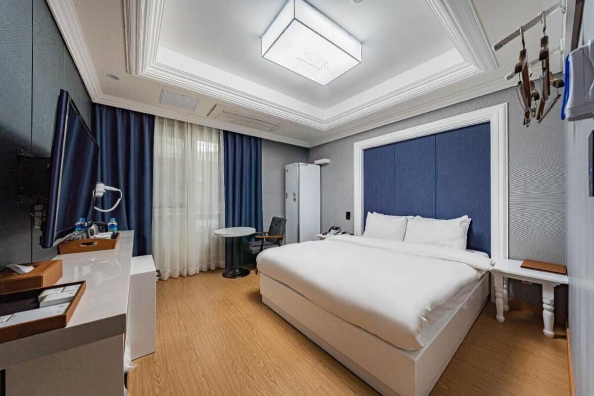 A hotel room with a large bed, a desk with a mirror, a small table, and a wardrobe.