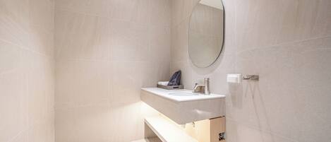 Un baño moderno con lavamanos, espejo y zona de ducha blancos.