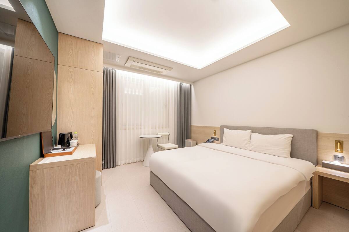 A modern hotel room with a large bed, a desk, a chair, and a small table.