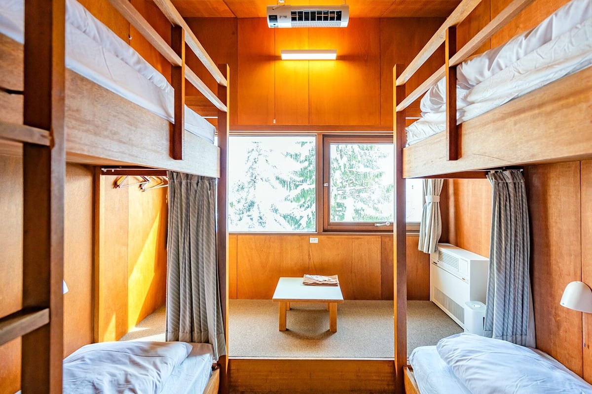 A cabin with bunk beds, a small table, and a window with a view of trees.