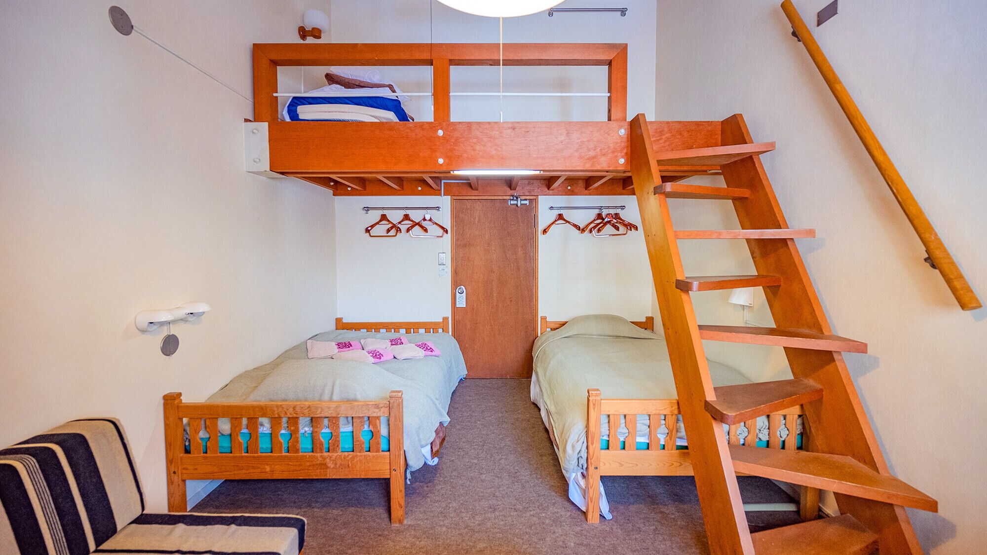 Habitación tipo dormitorio con dos camas, una litera, una escalera de madera y una pequeña zona de estar.