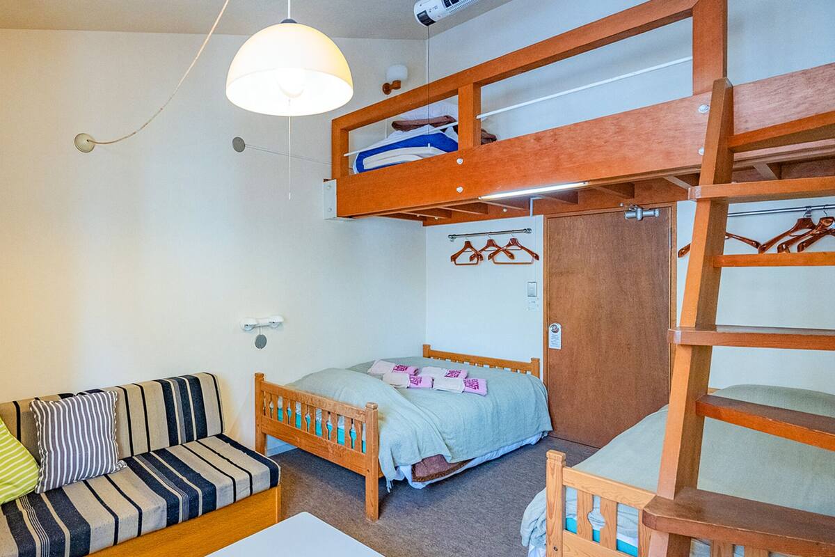 A compact room with a bunk bed, a sofa with striped cushions, a television, and a hanging light fixture.