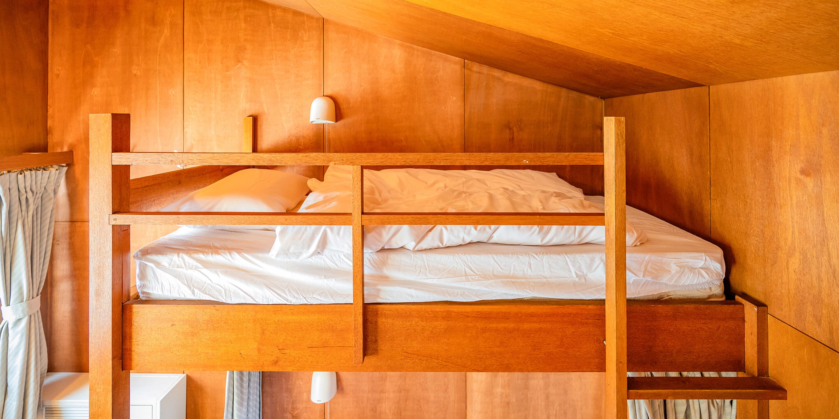 Un lit superposé en bois à deux niveaux, avec une literie blanche et deux lampes de chevet.