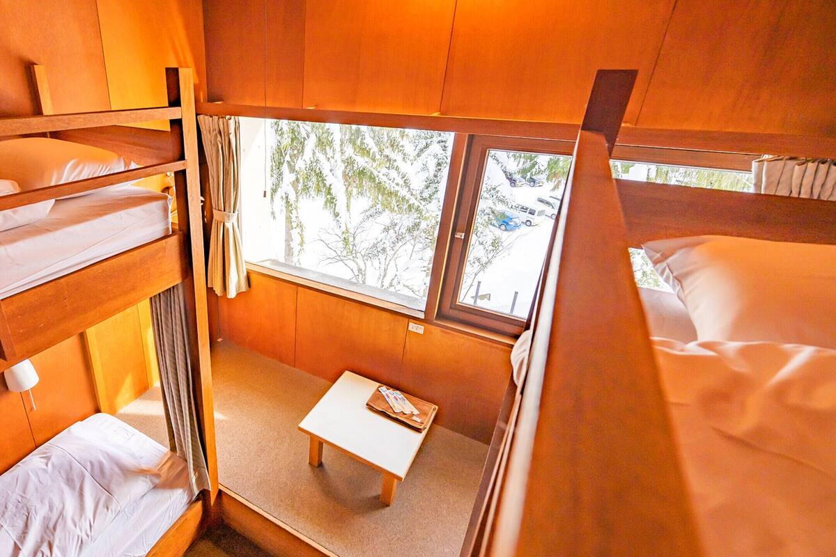 A bunk bed room with a small table and a window.