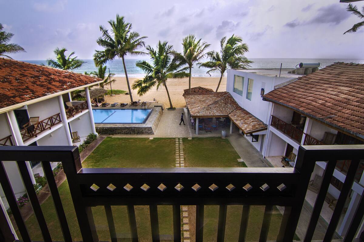 A view from a balcony overlooking a pool, a beach, and palm trees.