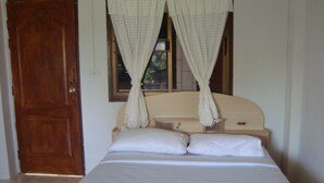 Uma cama de solteiro com roupa de cama branca e um dossel, uma porta de madeira e uma janela com cortinas.