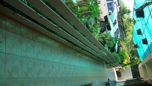 Uma área de pátio com piso de azulejos e guarda-corpo de metal, cercada por vegetação e um veículo estacionado.