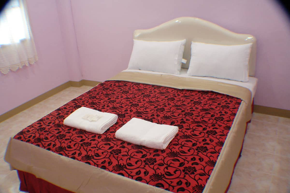 A neatly made bed with a red and black patterned bedspread, white pillows, and two folded white towels on the bed.
